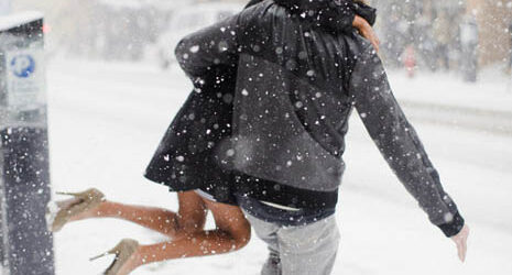 Young man carrying young woman across street in snow storm